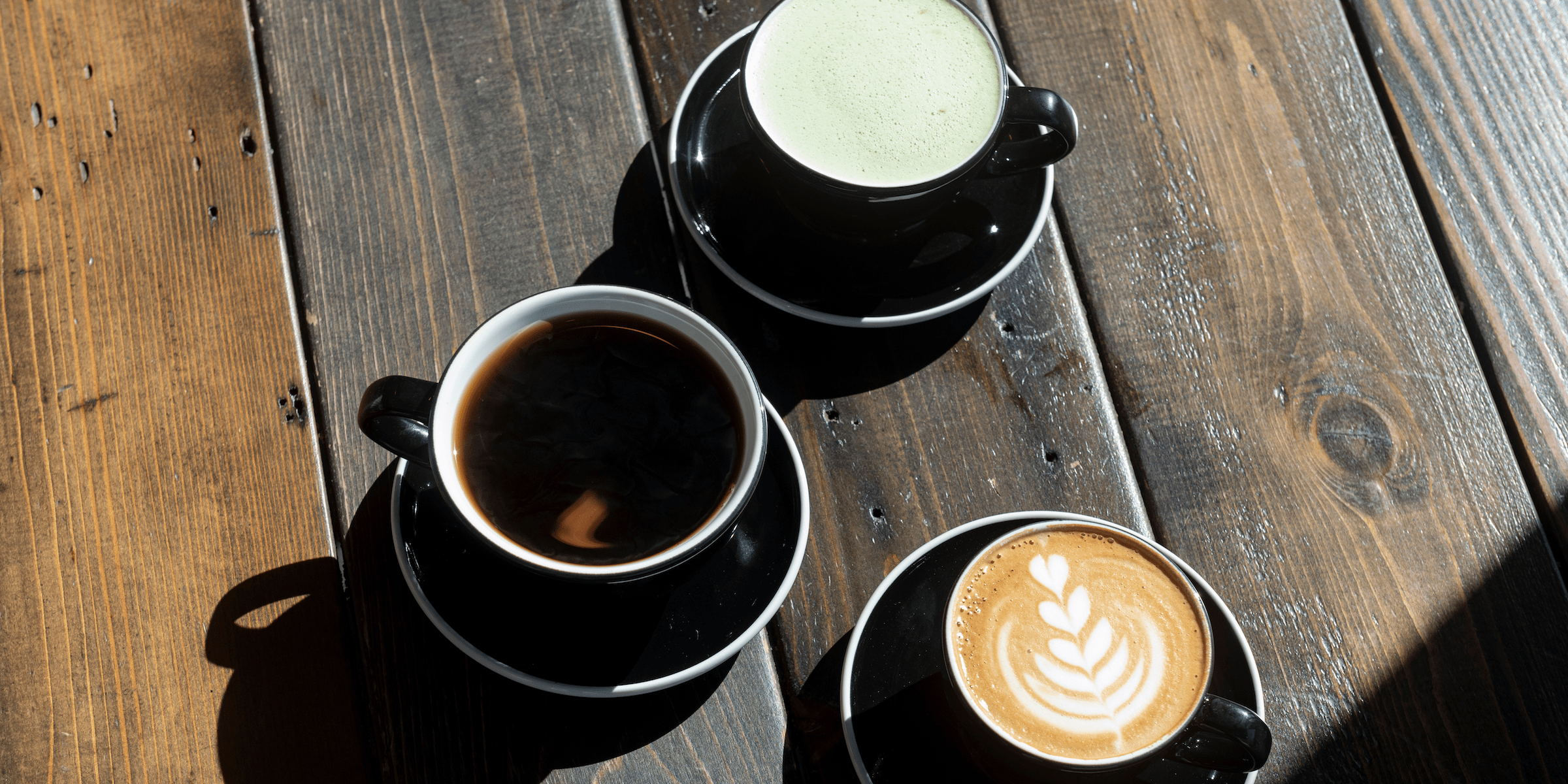 Three cups of espresso drinks sitting on a wooden table